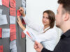 Eine Schulungsleiterin sortiert Brainstorming-Karten an einer Metaplanwand.