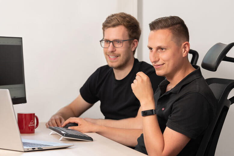 Zwei SAP-Verantwortliche sitzen gemeinsam an einem Schreibtisch mit PC, um SAP EWM Customizing zu lernen.
